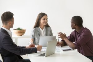 Um homem branco, um homem negro e uma mulher branca, sentados, reunidos para trabalhar