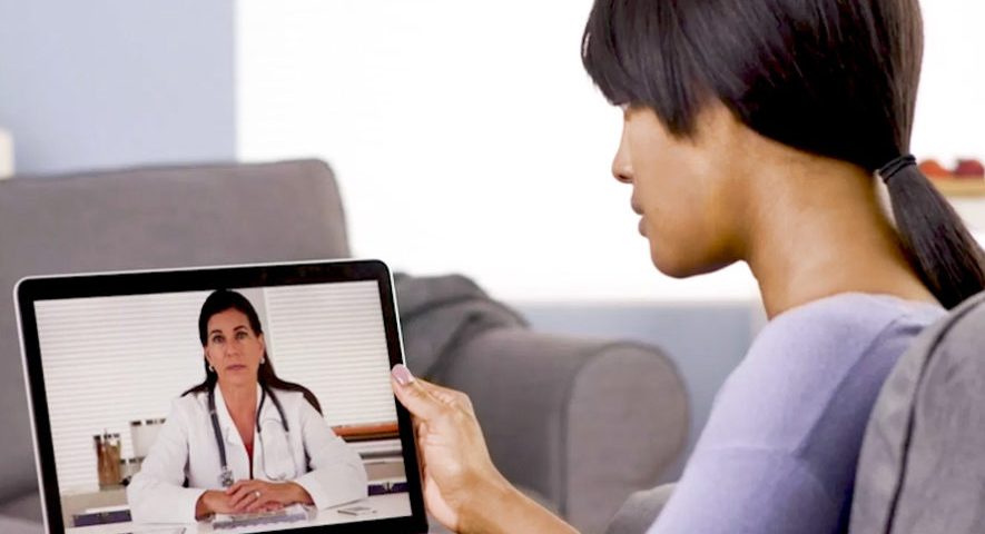 Mulher sentada falando com médica via teleconsulta por tablet